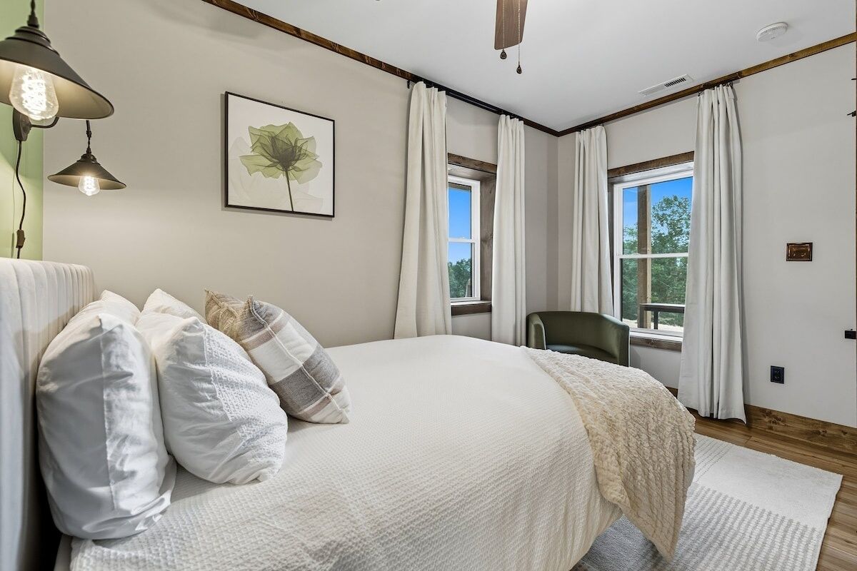 A bedroom with a large bed, a framed artwork, and a window with curtains.