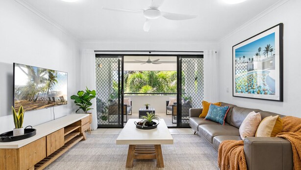 Un salon moderne comprenant un coin repas, un canapé, un téléviseur et un balcon offrant une vue sur la verdure.