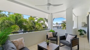 Un balcon doté d’un ventilateur de plafond, de deux fauteuils, d’une petite table et d’une plante en pot.