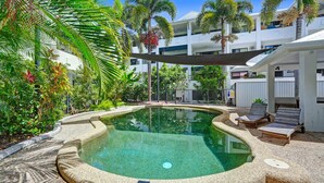 Une piscine à bord incurvé, entourée de chaises longues et de palmiers, avec un bâtiment en arrière-plan.