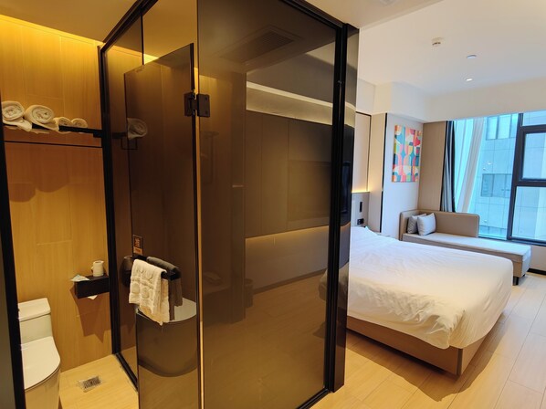 Une chambre d’hôtel dotée d’une douche en verre, d’un lit, d’un canapé et offrant une vue sur la ville grâce à de grandes fenêtres.