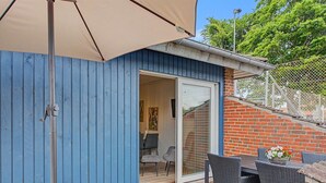 A blue wooden deck with a sliding glass door leading to an interior space, a table with chairs, and a potted plant.