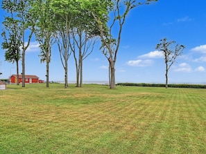 Un champ verdoyant, parsemé d’arbres, avec un bâtiment rouge en arrière-plan.