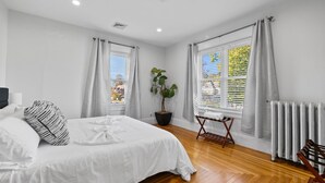 Un dormitorio con cama, planta en maceta, radiador y ventana con cortinas.