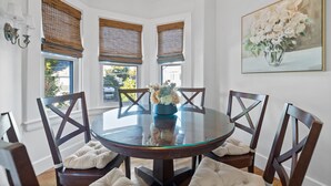 Un comedor con una mesa redonda de vidrio, sillas de madera oscura y un jarrón de flores.
