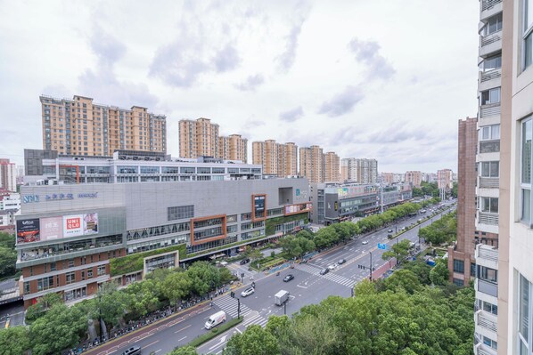 A modern urban street with high-rise buildings, a multi-story commercial building with large windows, and a busy intersection. - Tyms Family 4BR 2BA APT Residence (Shanghai)