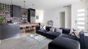 A modern kitchen with a bar area, a dark-colored sofa with patterned cushions, and a glass coffee table. - Modern Oasis: Rooftop Sunsets & City Lights! (Nashville)