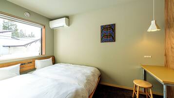 Un dormitorio con cama, escritorio, taburete, aire acondicionado, un cuadro y ventana.