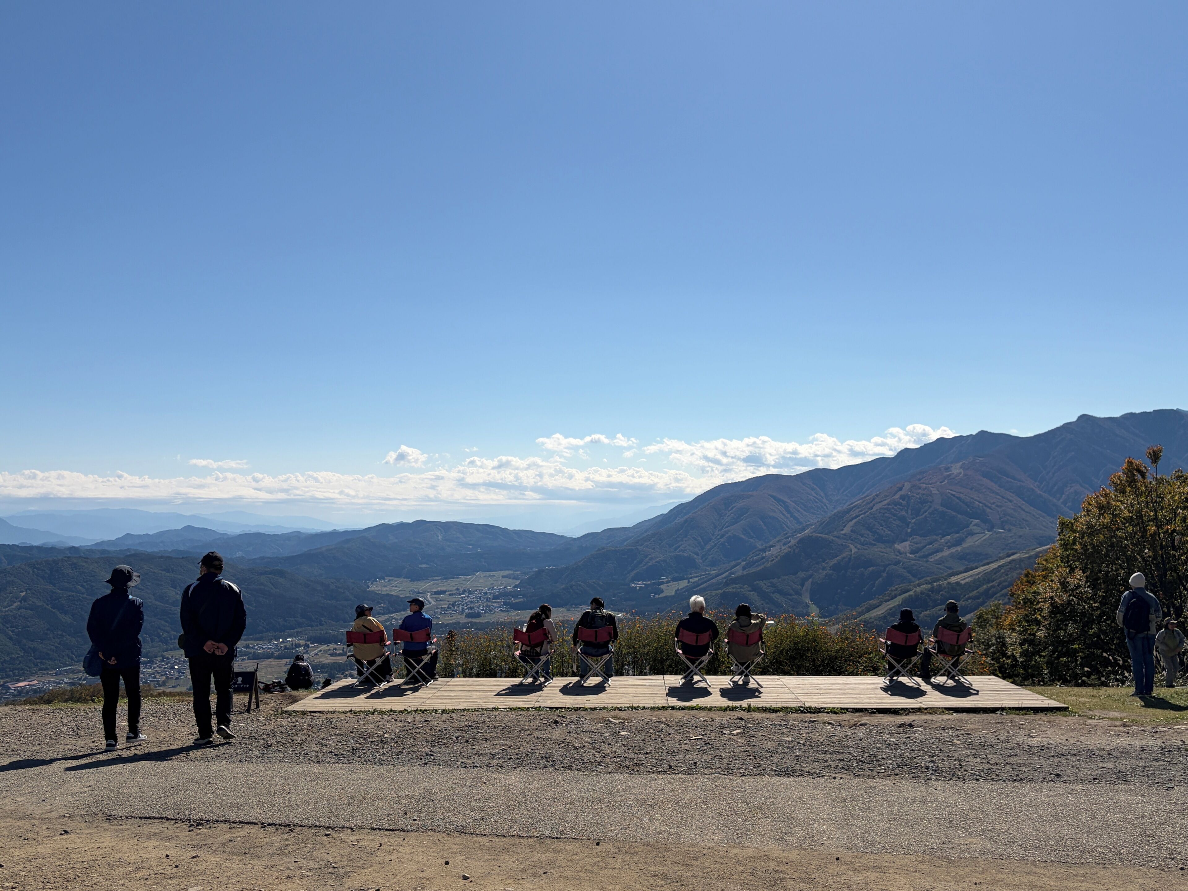 A group of people seated on a wooden platform with a scenic mountain view in the background.