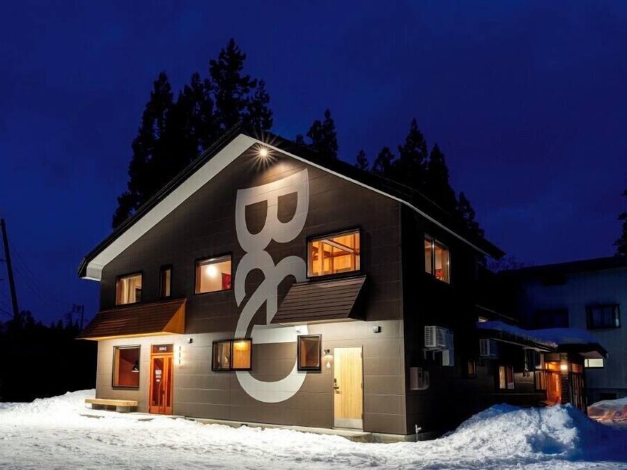 A modern two-story building with a large logo on the facade, multiple windows, and a snow-covered ground.