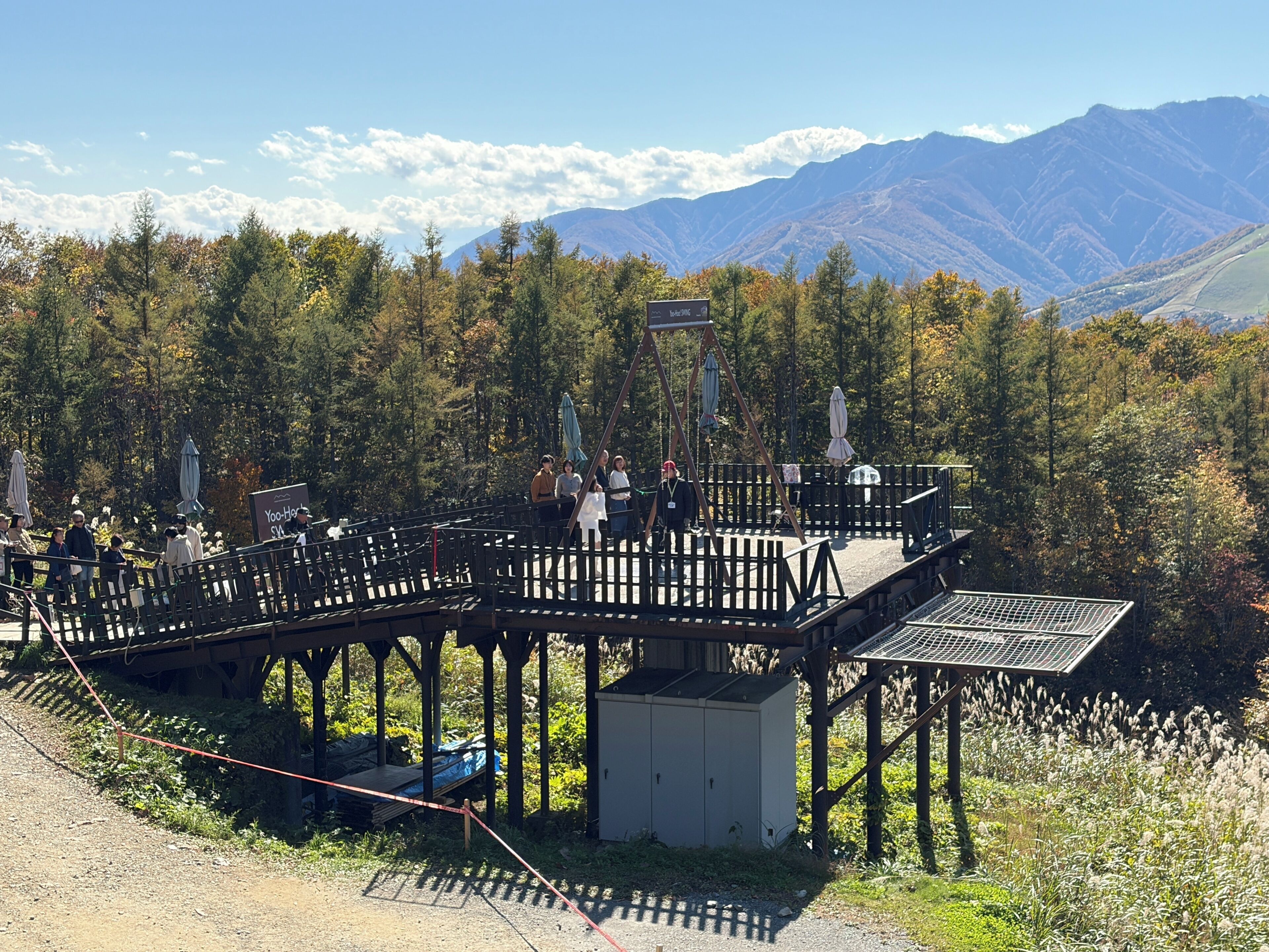A wooden deck with a metal roof, surrounded by trees and mountains.