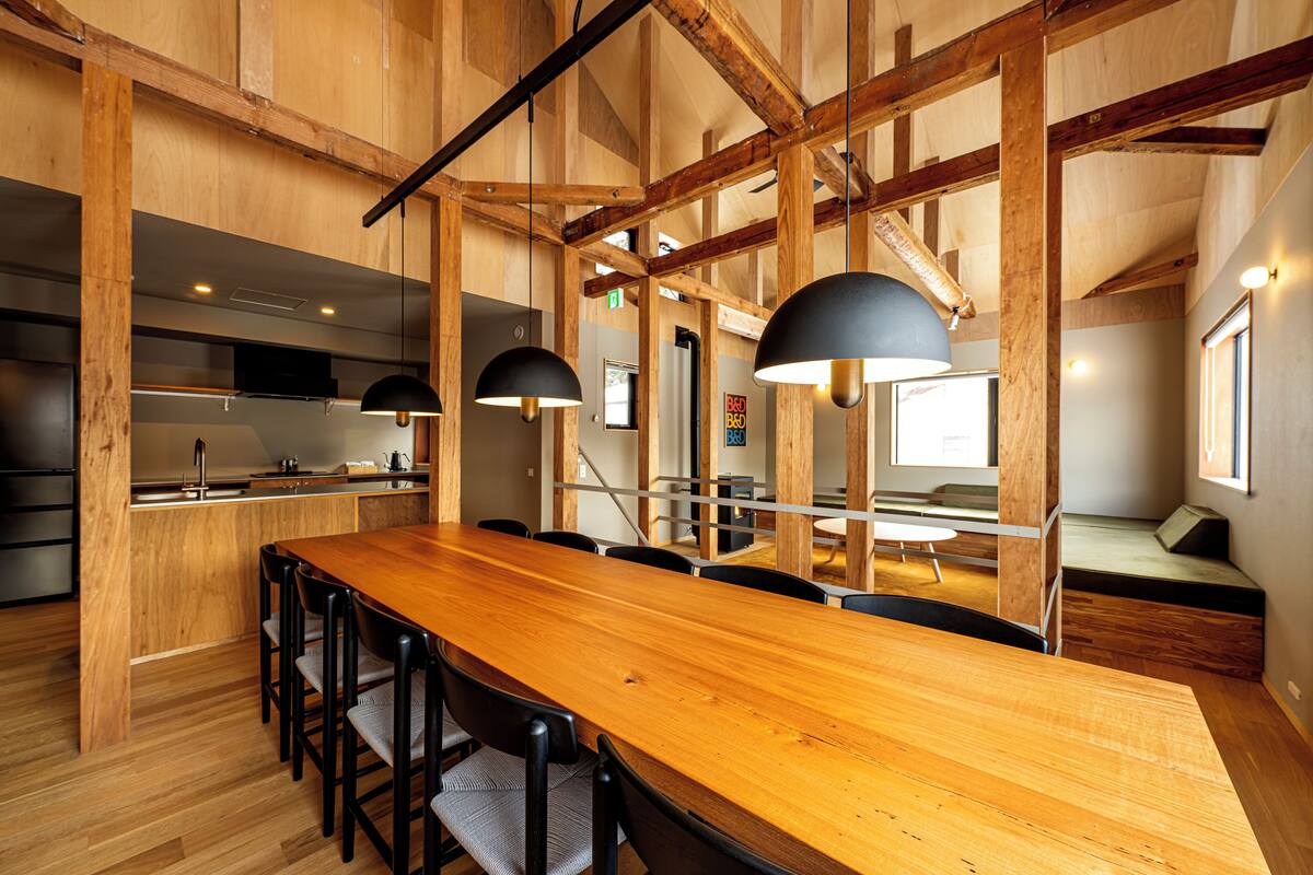 Una cocina moderna con una mesa y sillas de madera, estufa empotrada y lámparas colgantes.