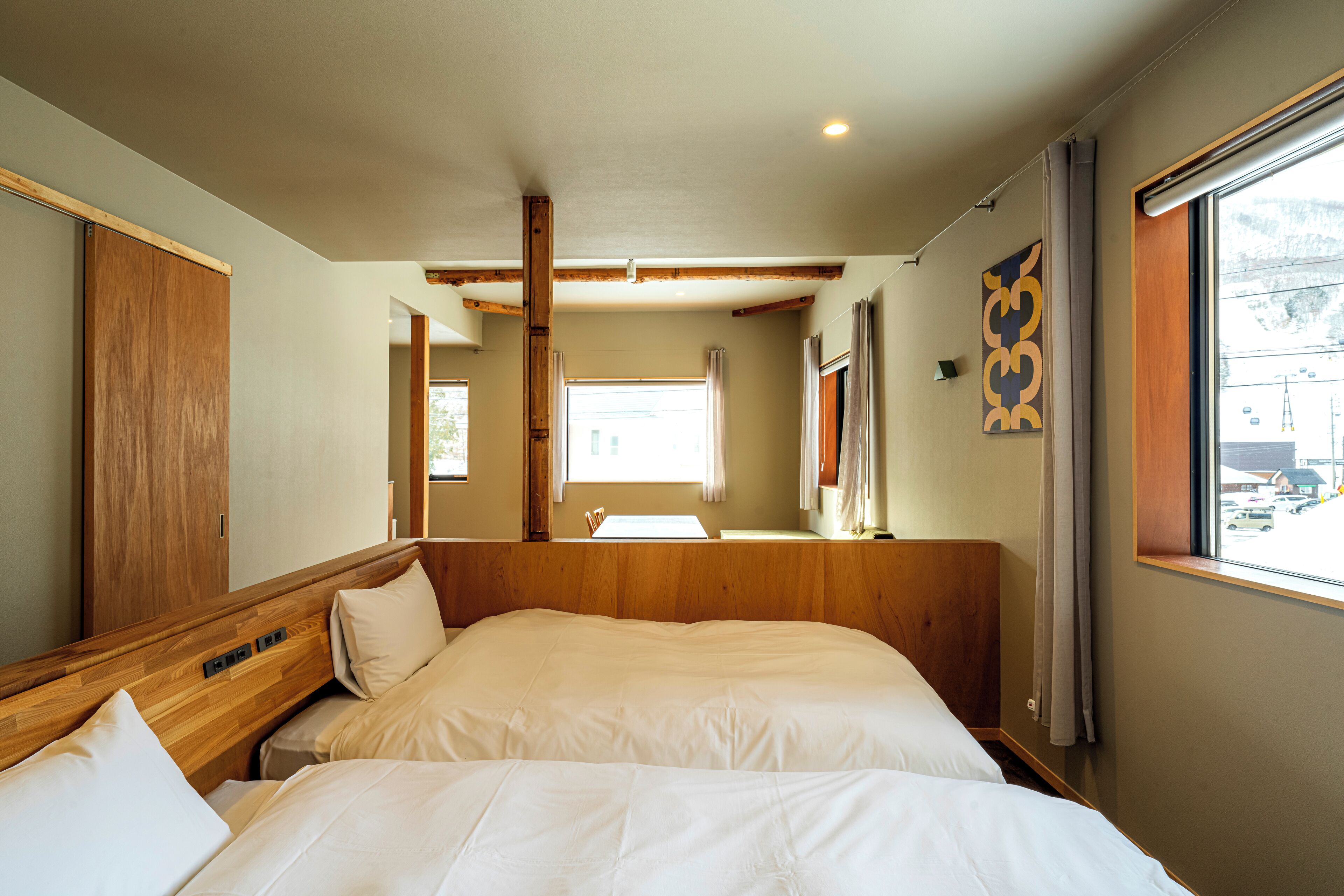 A hotel room with a wooden headboard, a large bed, a window with curtains, and a view of the outside.