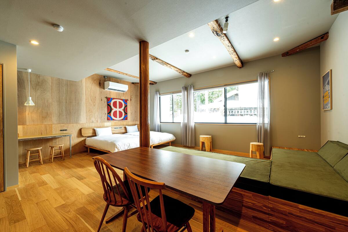 Una habitación moderna con una mesa de comedor de madera, sillas, una cama, un sofá verde y una ventana con cortinas.