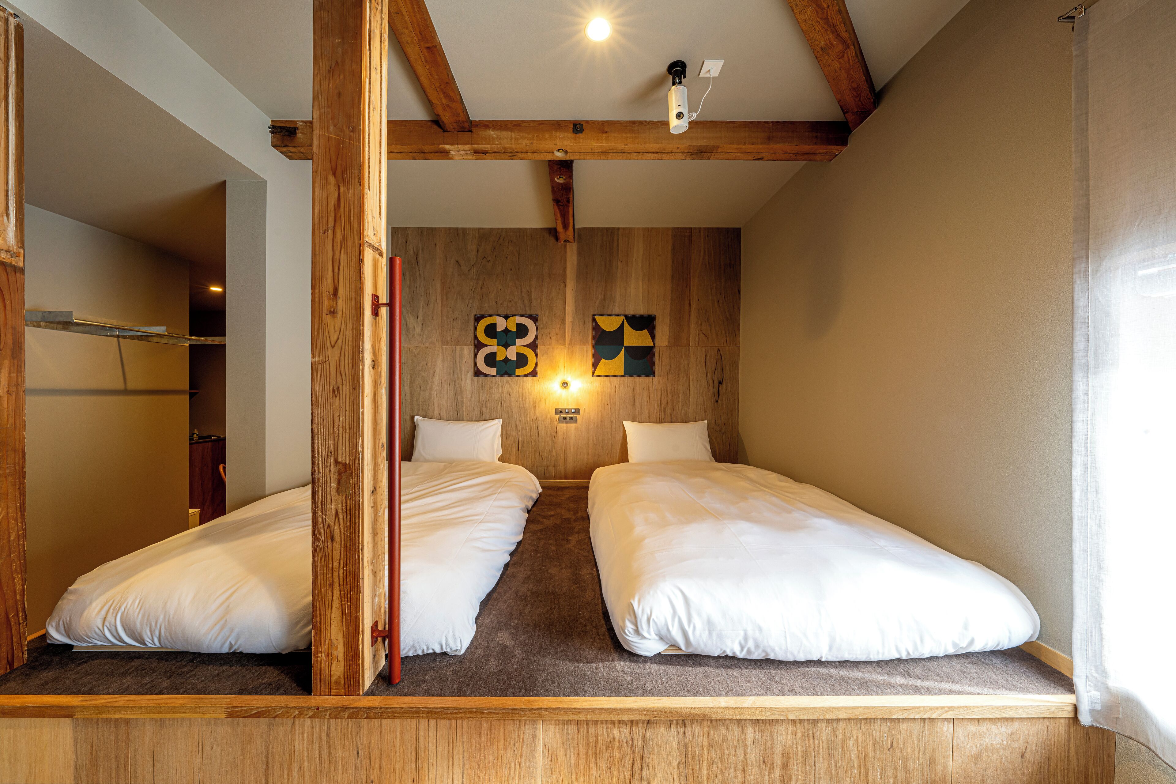 A room with two single beds, wooden beams on the ceiling, and artwork on the wall.