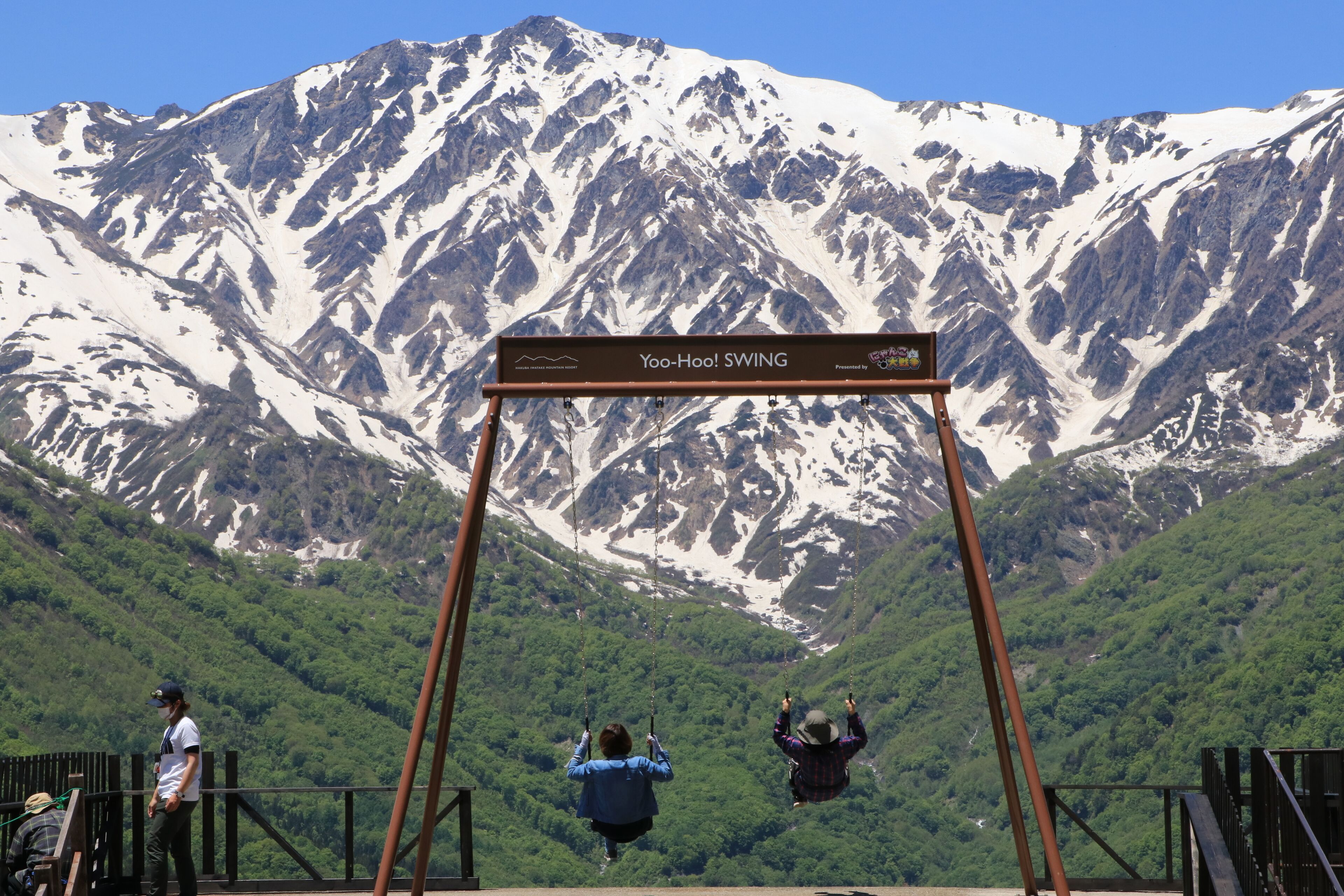 Un conjunto de columpios con un cartel que dice "Yoo-Hoo! SWING" frente a un paisaje montañoso.