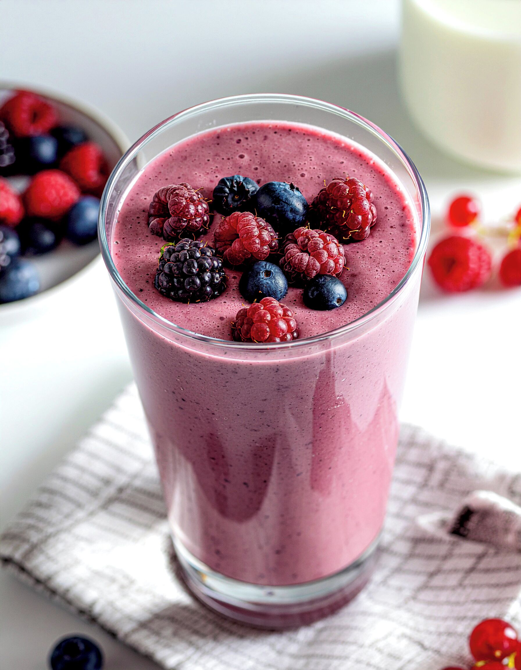 Un vaso de batido con frutos rojos encima, sobre un paño.