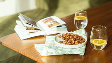 A wooden table with a bowl of nuts, two glasses of water with lemon slices, and an open magazine.