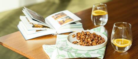 A wooden table with a bowl of nuts, two glasses of water with lemon slices, and an open magazine.