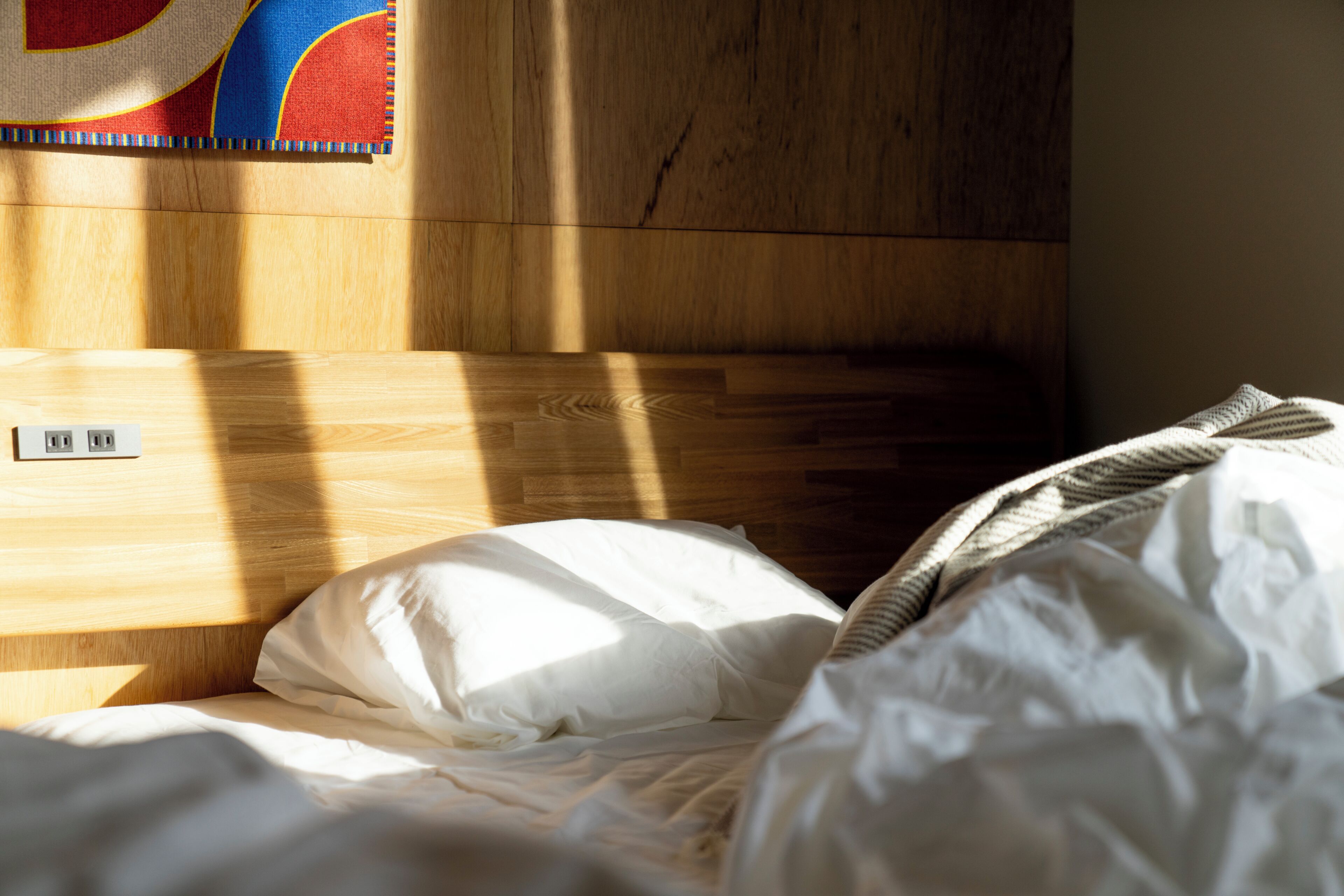 Een houten hoofdbord, een stopcontact en een bed met witte lakens.