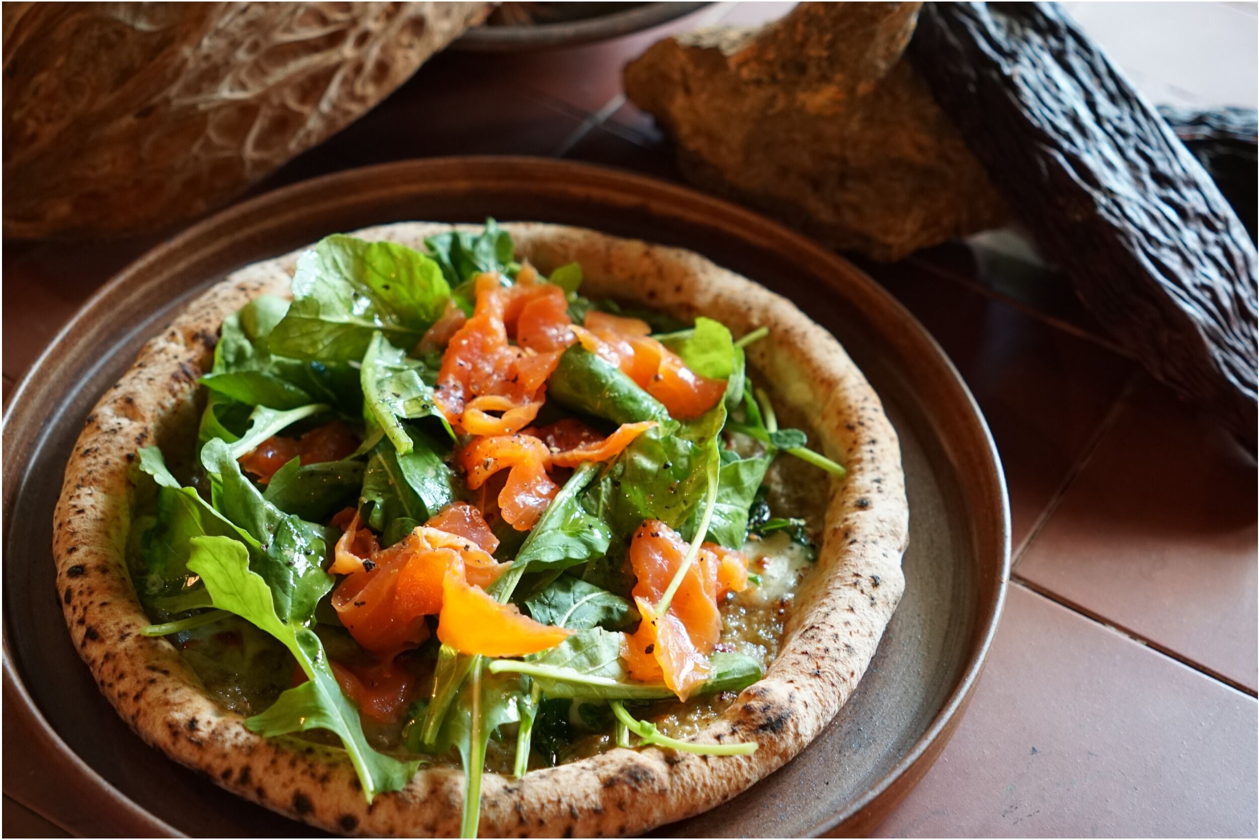 A pizza with a crispy crust, topped with fresh greens and slices of tomato.