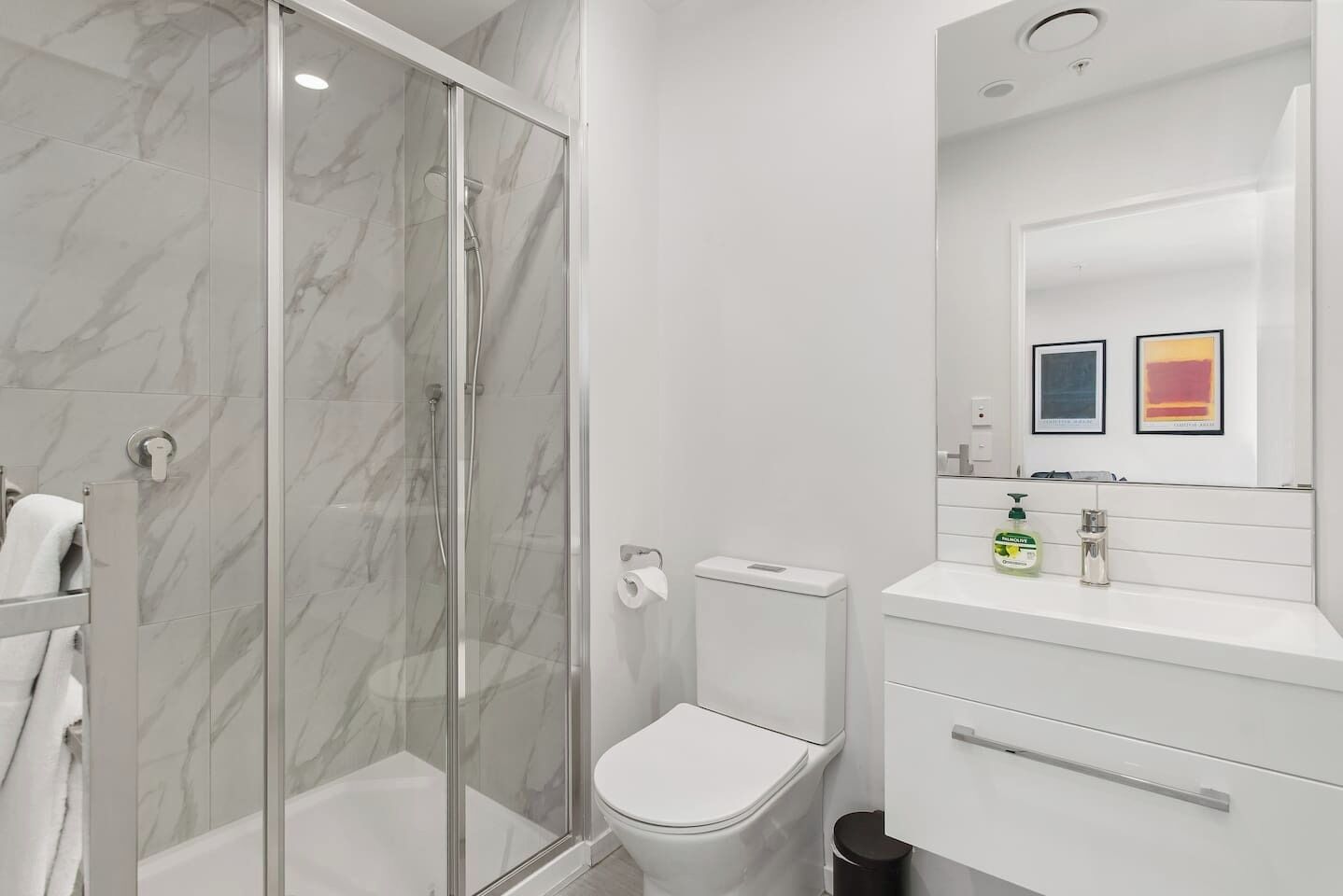 Un baño moderno con ducha de vidrio, inodoro y tocador con espejo.