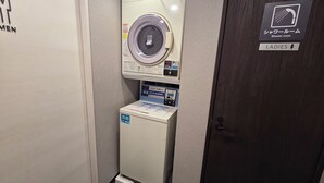 Een kleine wasruimte met een wasmachine en droger, een bordje voor de douche ruimte en een bordje dames.