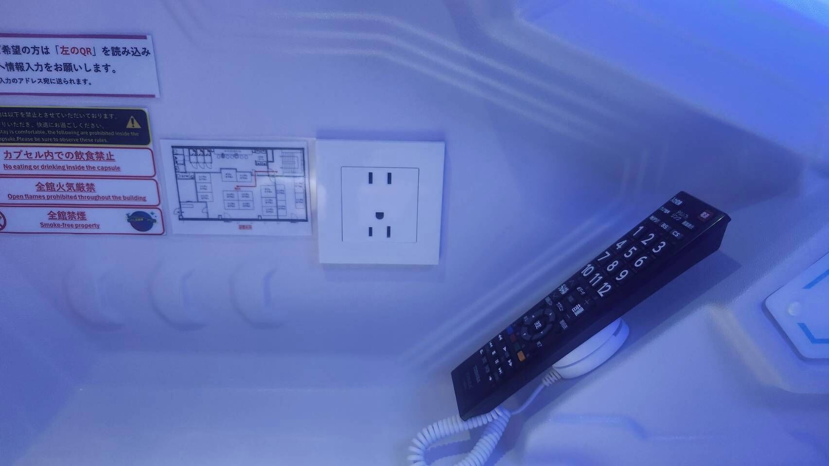 Een afstandsbediening, een stopcontact en veiligheidssignes op een muur.