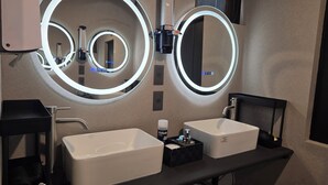 Een moderne badkamer met twee wastafels, een grote spiegel met ingebouwde verlichting, en een kleine spiegel boven de wastafel.