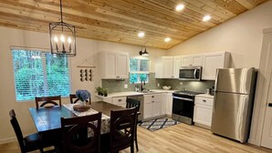 A modern kitchen with wooden flooring, white cabinets, stainless steel appliances, and a dining area with a table and chairs. - Charming 2-bedroom cottage with a hot tub. 5 Min to Volcanoes National Park! (Volcano)
