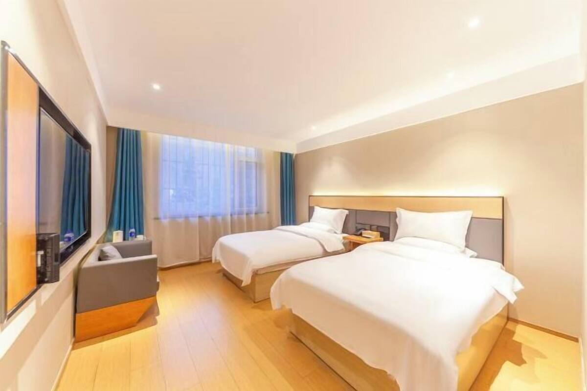 A hotel room with two beds, a desk, a chair, and a large window with curtains.