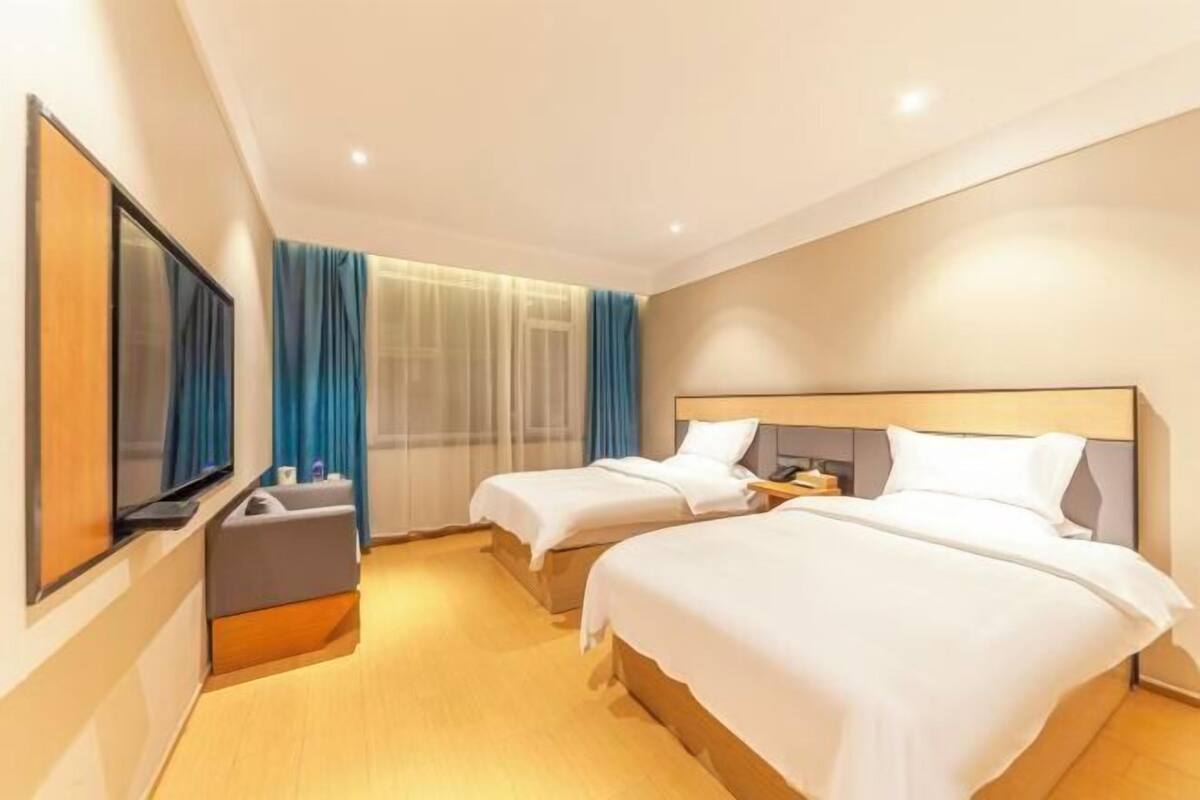 A hotel room with two beds, a TV, a bedside table, and a window with curtains.