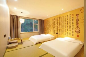 Habitación de hotel con esteras de tatami, dos camas, una ventana con cortinas, una mesita de noche con lámpara y una pared con caligrafía china.