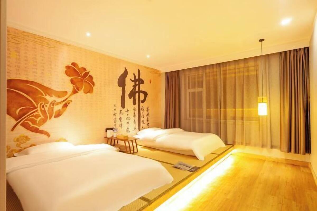 A hotel room with two beds, a large mirror, a wall with calligraphy, and a curtain-covered window.
