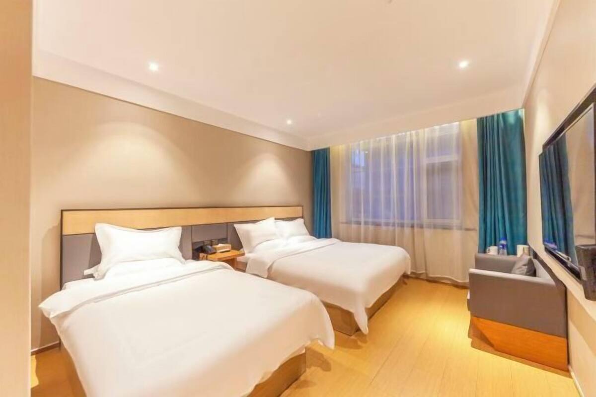 A hotel room with two beds, a TV, a desk, and a window with curtains.