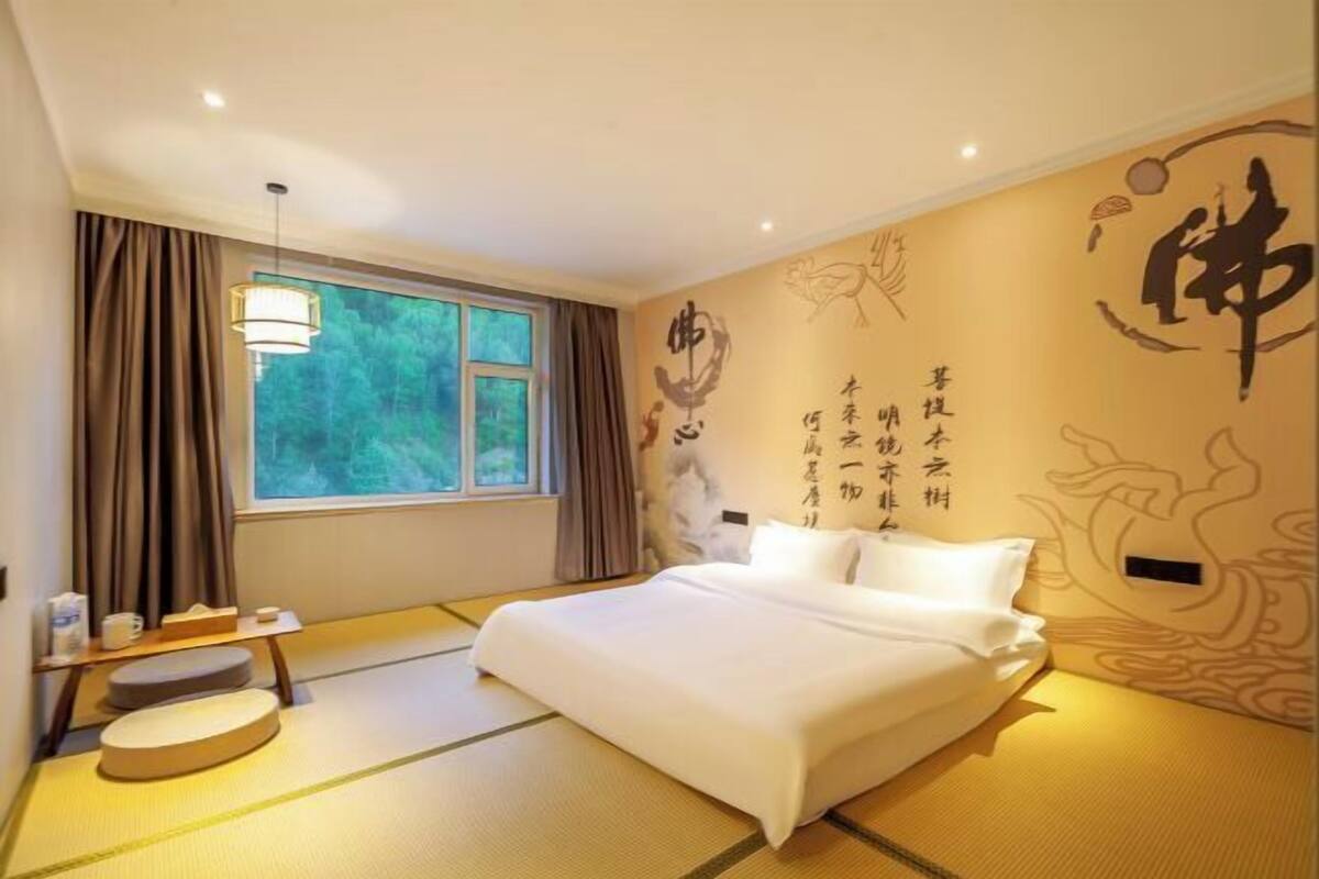 A room with tatami flooring, a bed, a window with curtains, a bedside table with a lamp, and decorative wall art.