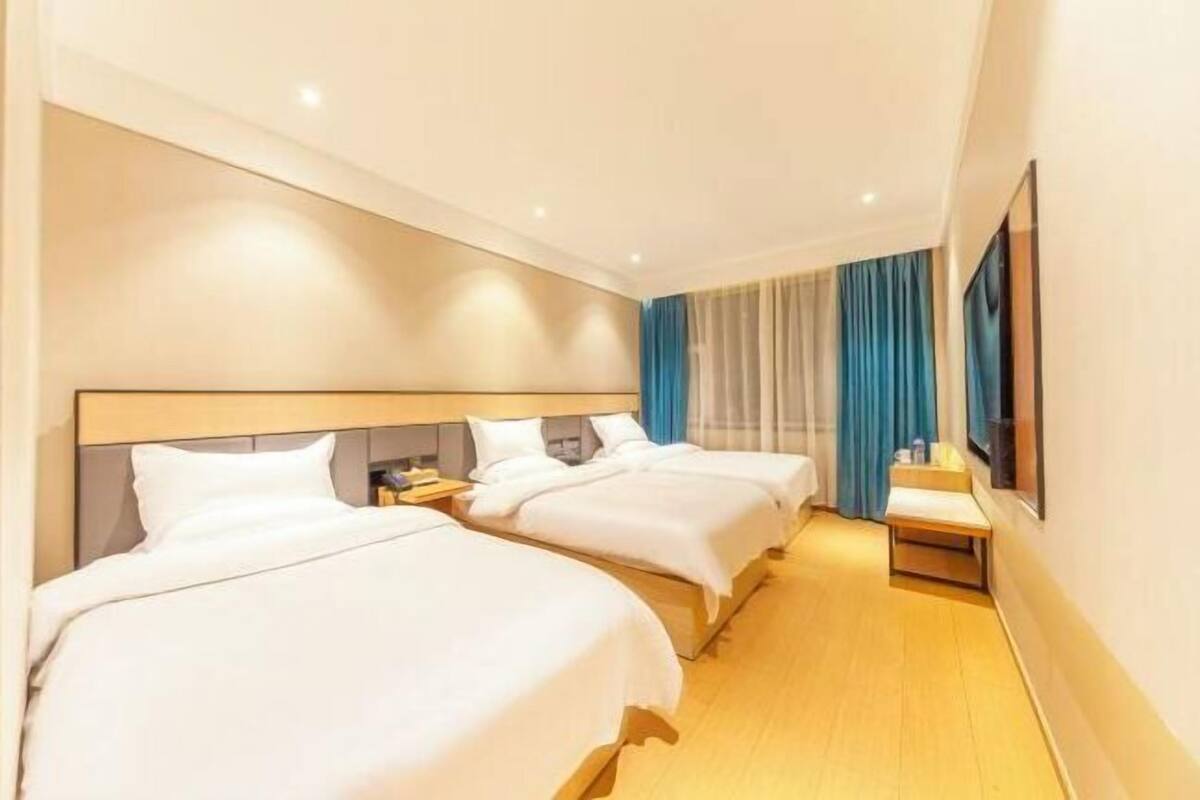A hotel room with three beds, a flat-screen TV, and a small table.