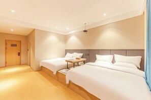 Una habitación de hotel con dos camas, piso de madera, una lámpara en el techo y una puerta.