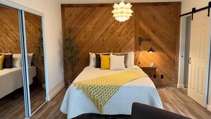 A bedroom with a large bed, wooden walls, a hanging light fixture, and a bedside table with a lamp. - The White Door Studio. (Lutz)