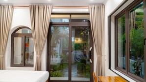 A bedroom with a bed, a wooden table, and a sliding glass door leading to a garden.