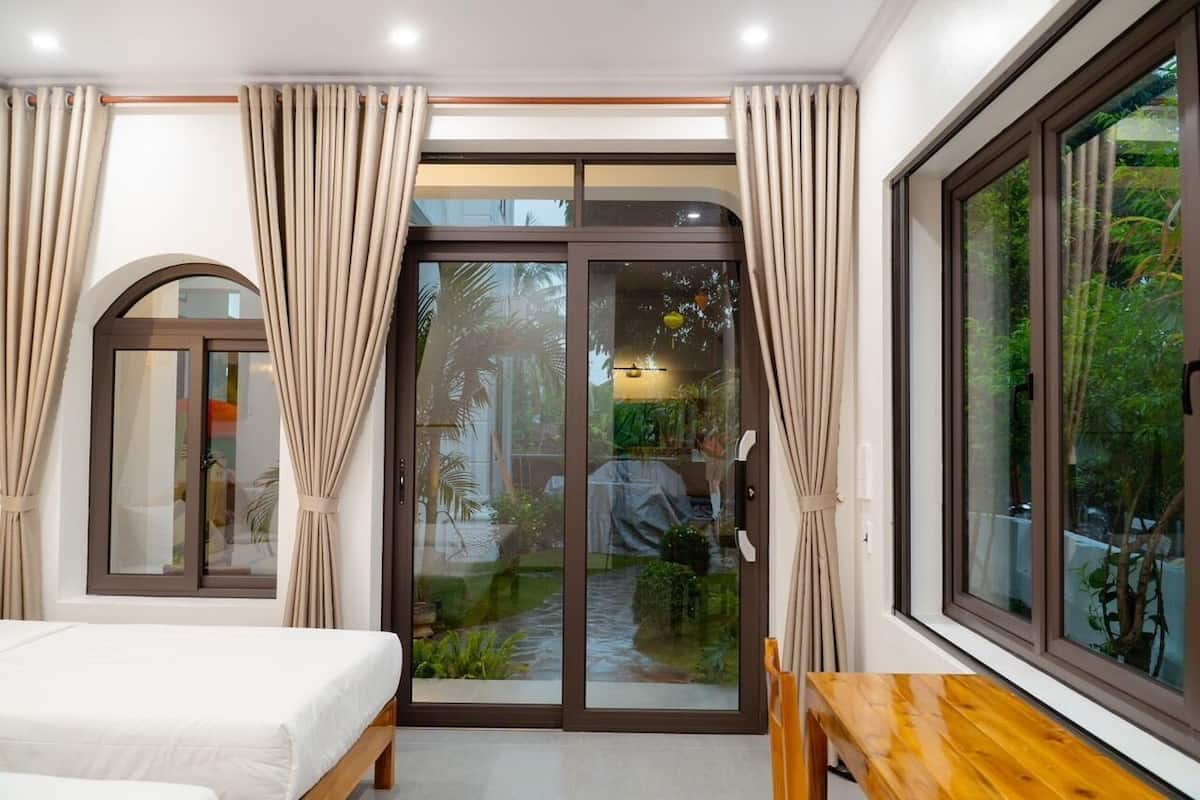 A bedroom with a bed, a wooden table, and a sliding glass door leading to a garden.