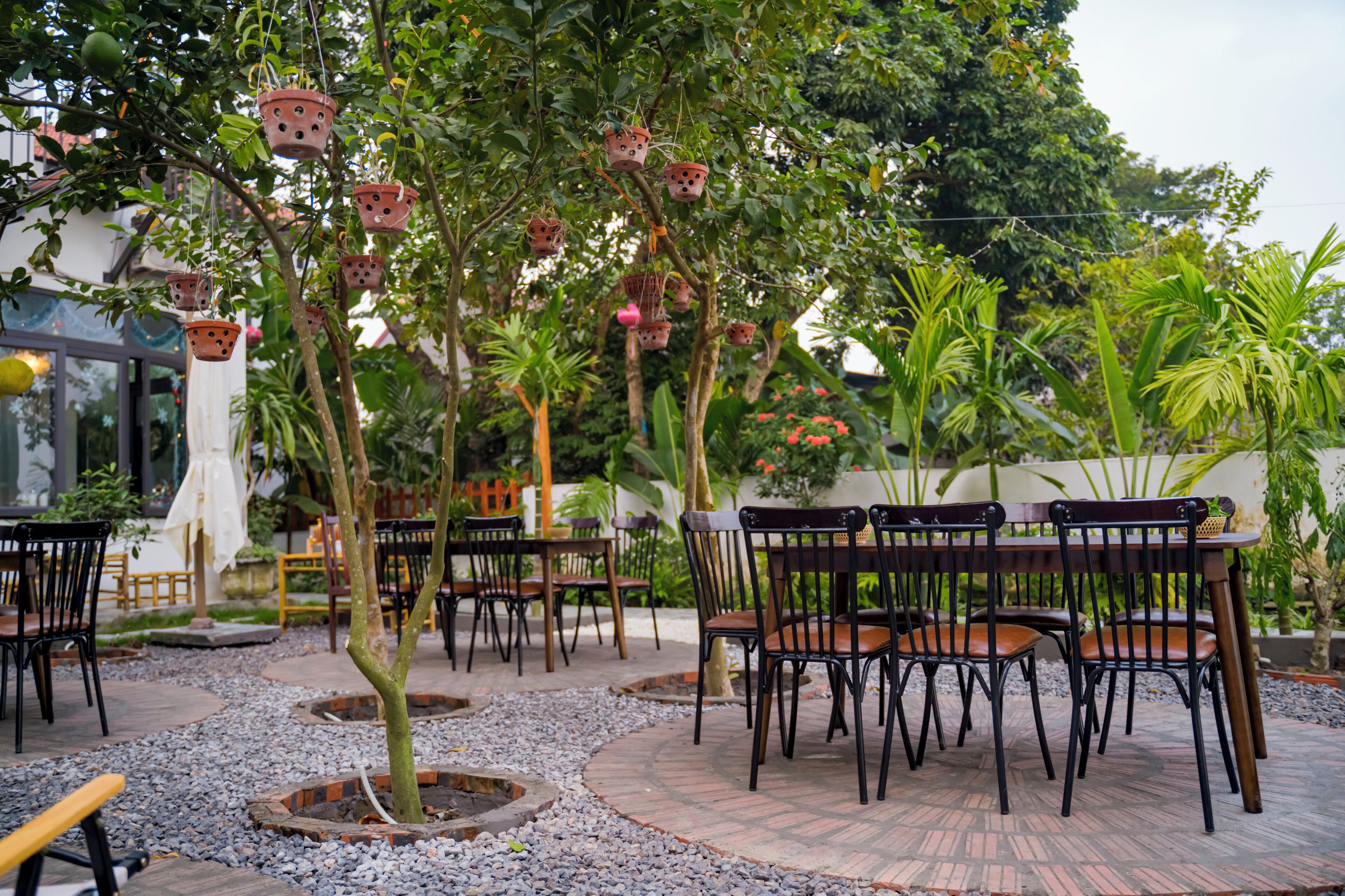 An outdoor seating area with tables and chairs, surrounded by trees and plants.