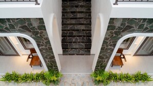 A modern staircase with stone steps and white walls, flanked by two wooden chairs and green plants.