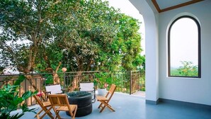 A balcony with a seating area, a potted plant, and a view of greenery.
