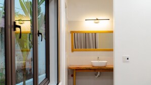 A modern bathroom with a large window, a wooden vanity, a white sink, and a mirror with a light above it.