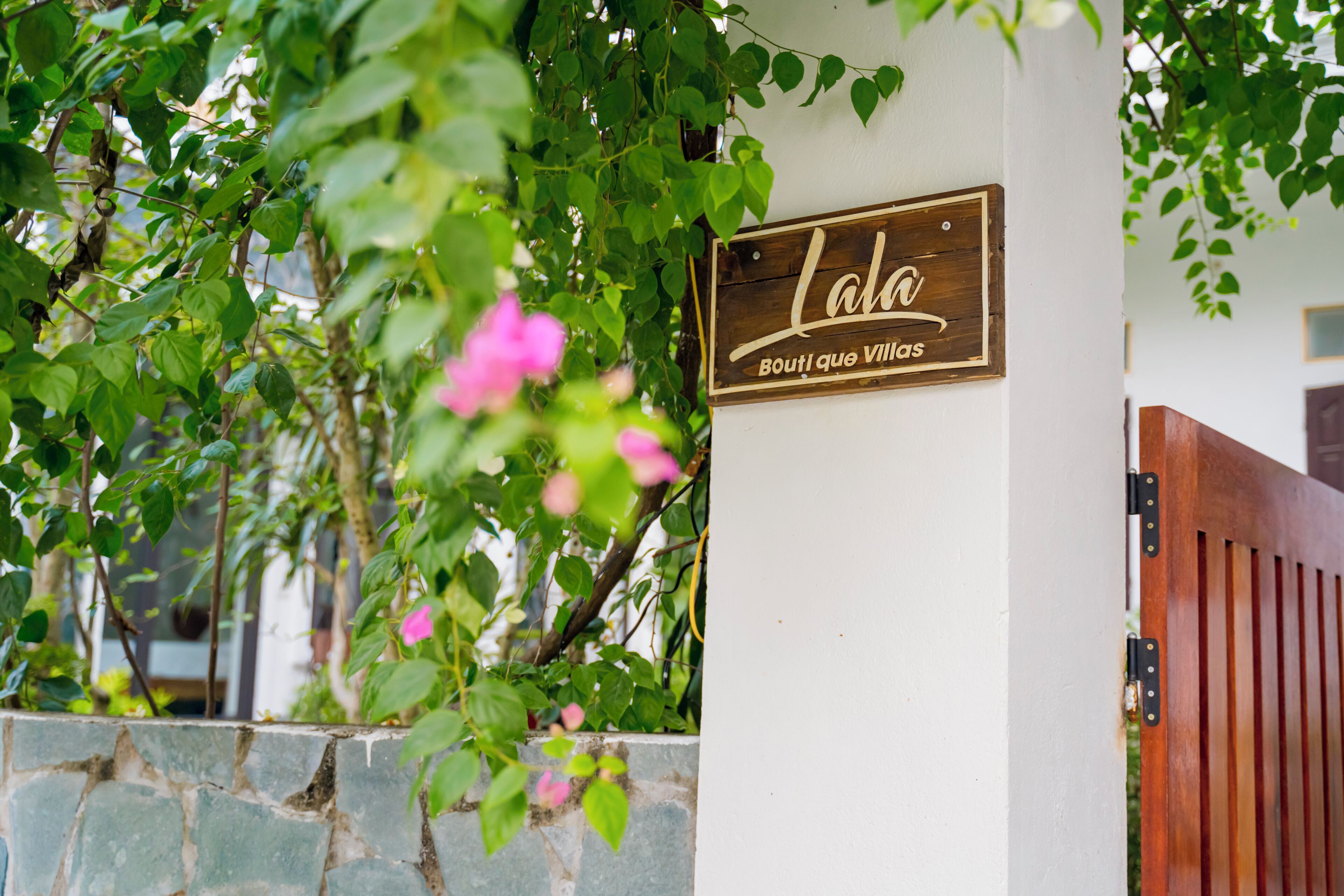 Uma placa de madeira com o nome 'Lala Boutique Village' numa parede branca.