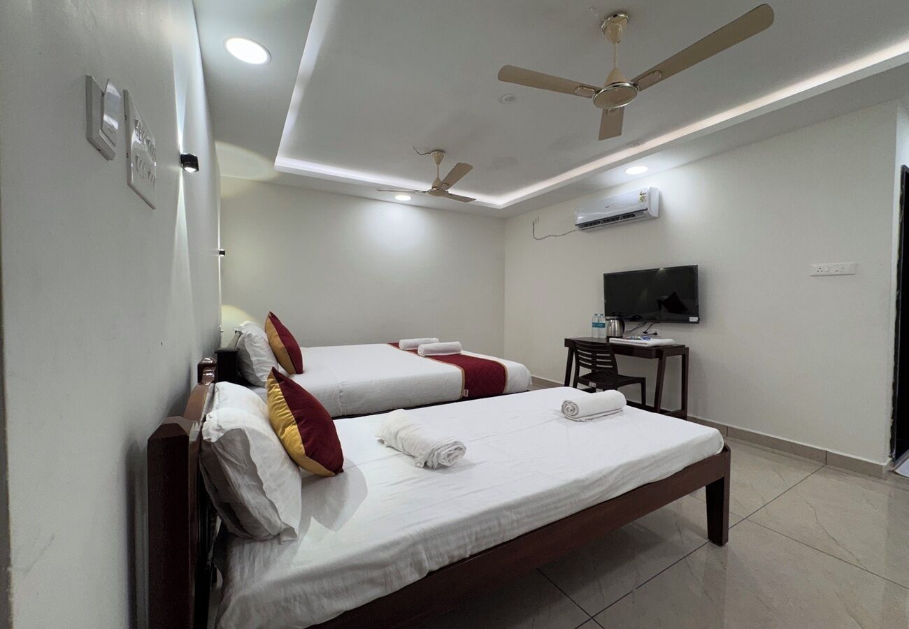Habitación de hotel con dos camas individuales, cabecera de madera, escritorio con silla, televisor de pantalla plana y ventiladores de techo.