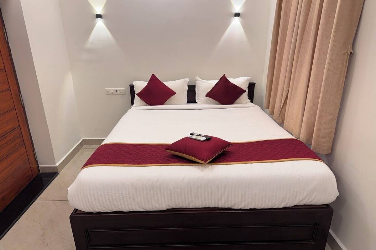 A neatly made bed with a white duvet, two red pillows, and a red throw blanket.