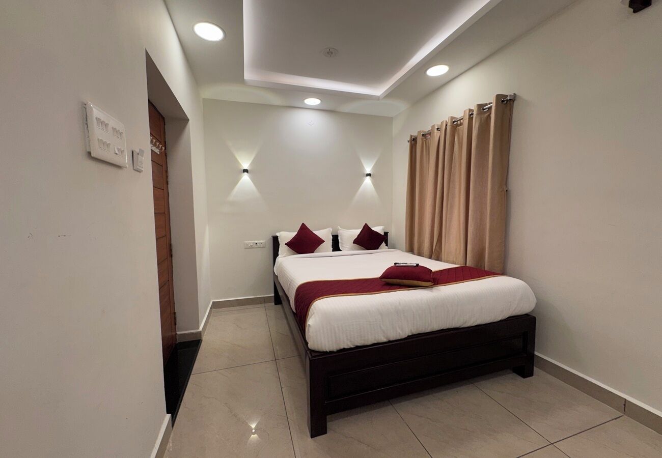 A bedroom with a bed, two wall-mounted lights, a window with curtains, and a door.