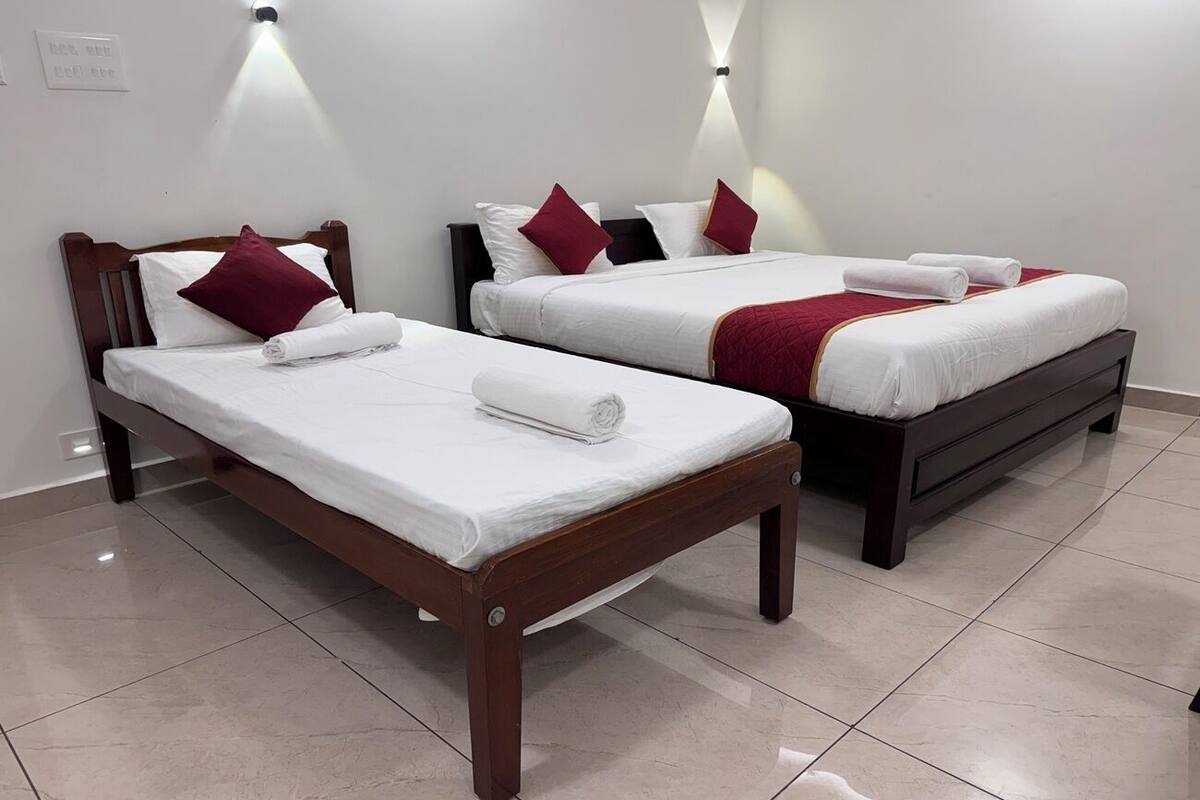 Two single beds with wooden frames and white bedding, each with a red pillow and a rolled towel.